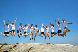 A large group of campers jumping up at the same time on top of a mountain