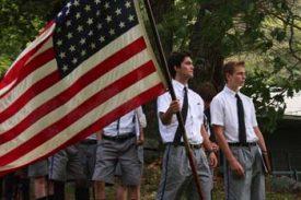 Three boys in white shirts and neckties holding an American flag