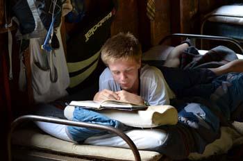Child relaxing in a cot reading at Camp Pasquaney
