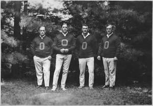 Four men standing outside in O letter sweaters at Camp Pemigewassett