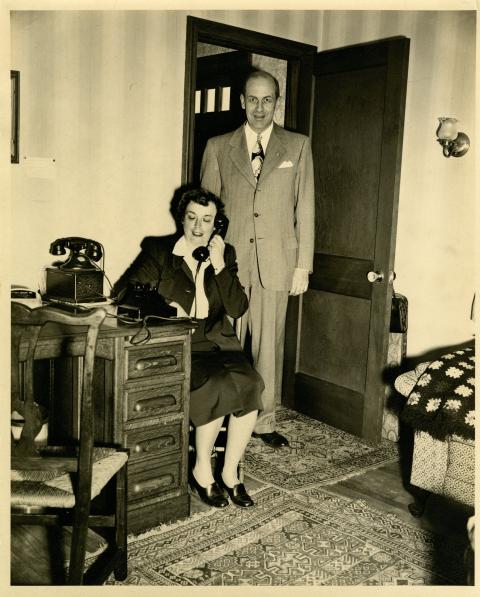 Photograph of man standing behind woman who is operating phone.