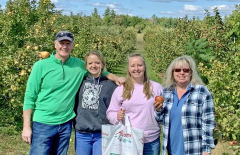 A photo of a man, Jack Cunnane, next to his wife and 2 daughters, standing in an apple orchard