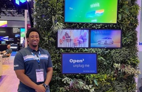 Photo of a man, Elijah Johnson, standing next to some tv displays at a professional conference